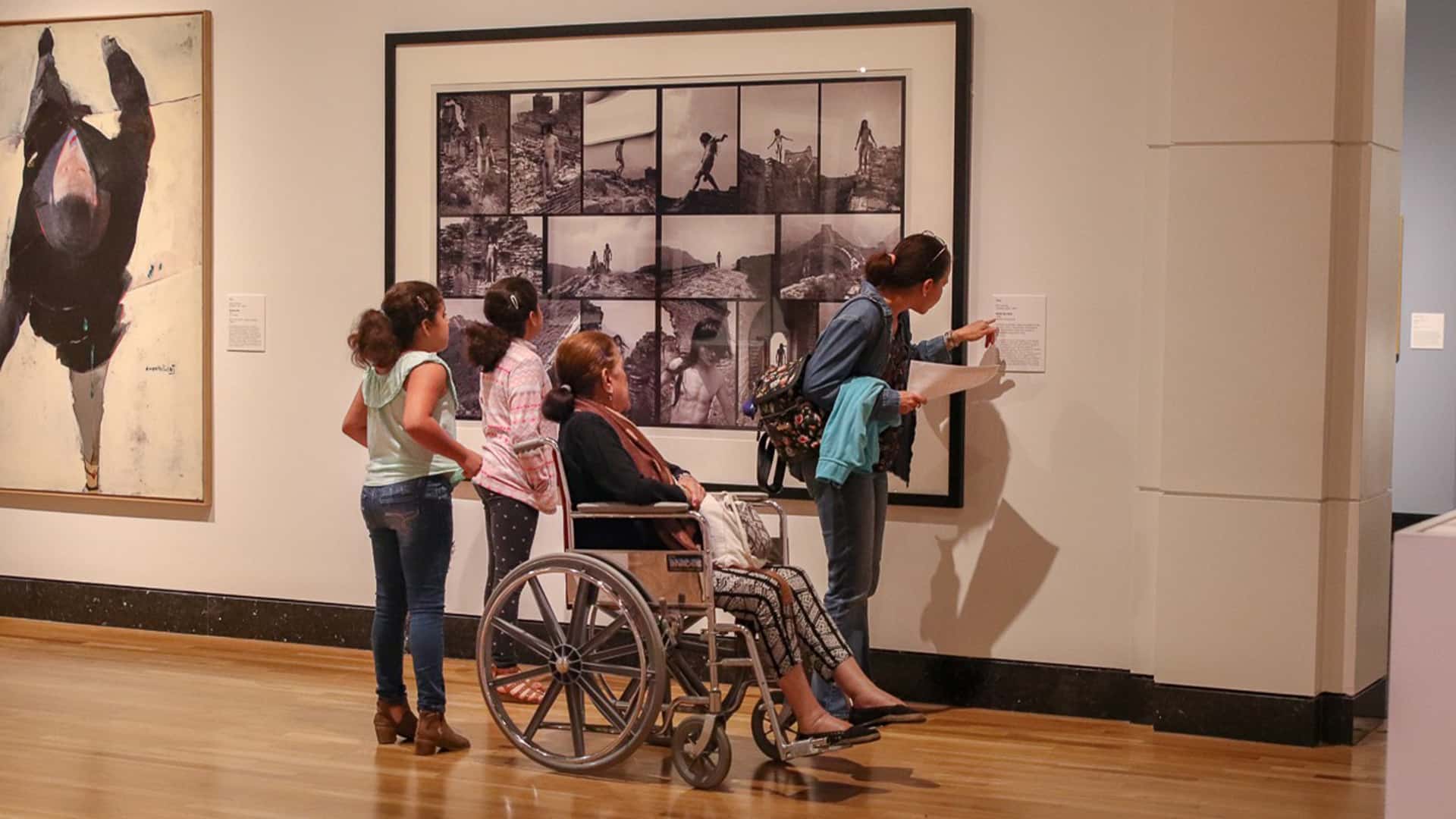 A group of visitors, one in a wheelchair, viewing art in a gallery.