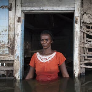 Adlene Pierre, aged 35, faces the camera in the doorway of her flooded house in Savanne Desole on the outskirts of the city of Gonaives. She had lost most of her possessions. Two weeks earlier the entire city had been flooded during Hurricanes Ike and Hanna and at this point this was the last remaining district still engulfed. Hundreds of people are said to have died as the La Quinte river burst its banks and devastated the city. During the hurricane season of 2008 Haiti was subjected to four powerful hurricanes in the space of twenty days. This increasing severity and quantity of hurricanes is one of the effects of climate change. But Haiti is extremely vulnerable to these extreme climatic events due to the deforestation of its hillsides. So during extreme rain conditions the ground does not hold the water causing mudslides and widespread flooding.