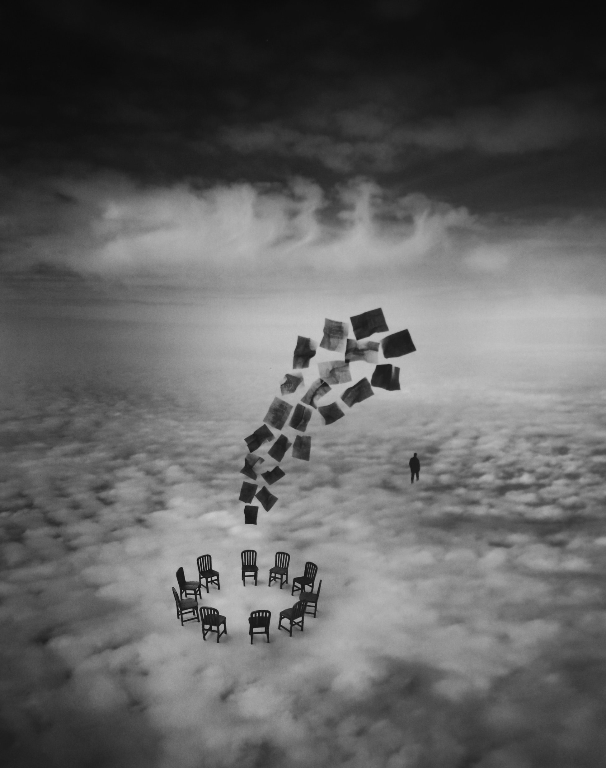 Jerry Uelsmann's "The Committee," 2002: a photo collage of a circle of chairs sitting on clouds, with a grouping of papers lifting from the center into the air, and a human figure off to the right