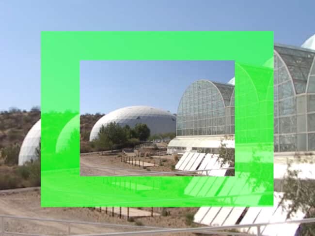 still image from a video of several rounded building with blue sky and a neon green thick frame in the center over the image