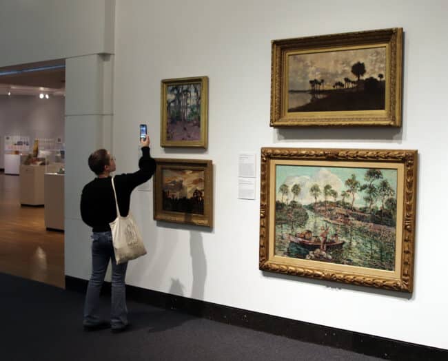 museum visitor taking a photo of a painting in the "Florida Impressions" exhibition