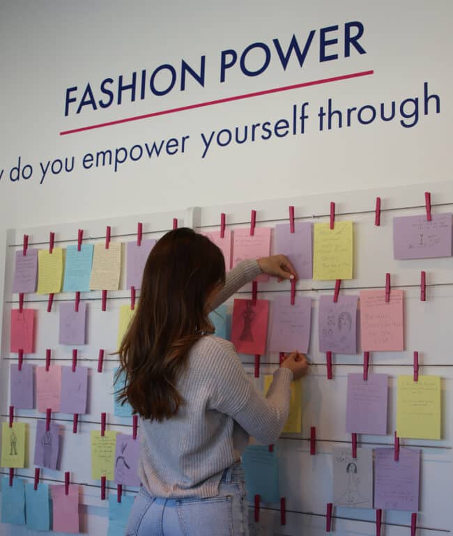 museum visitor hanging a note on the wall in the Fashion Power interactive within the "Ghanaian Fashion" exhibition