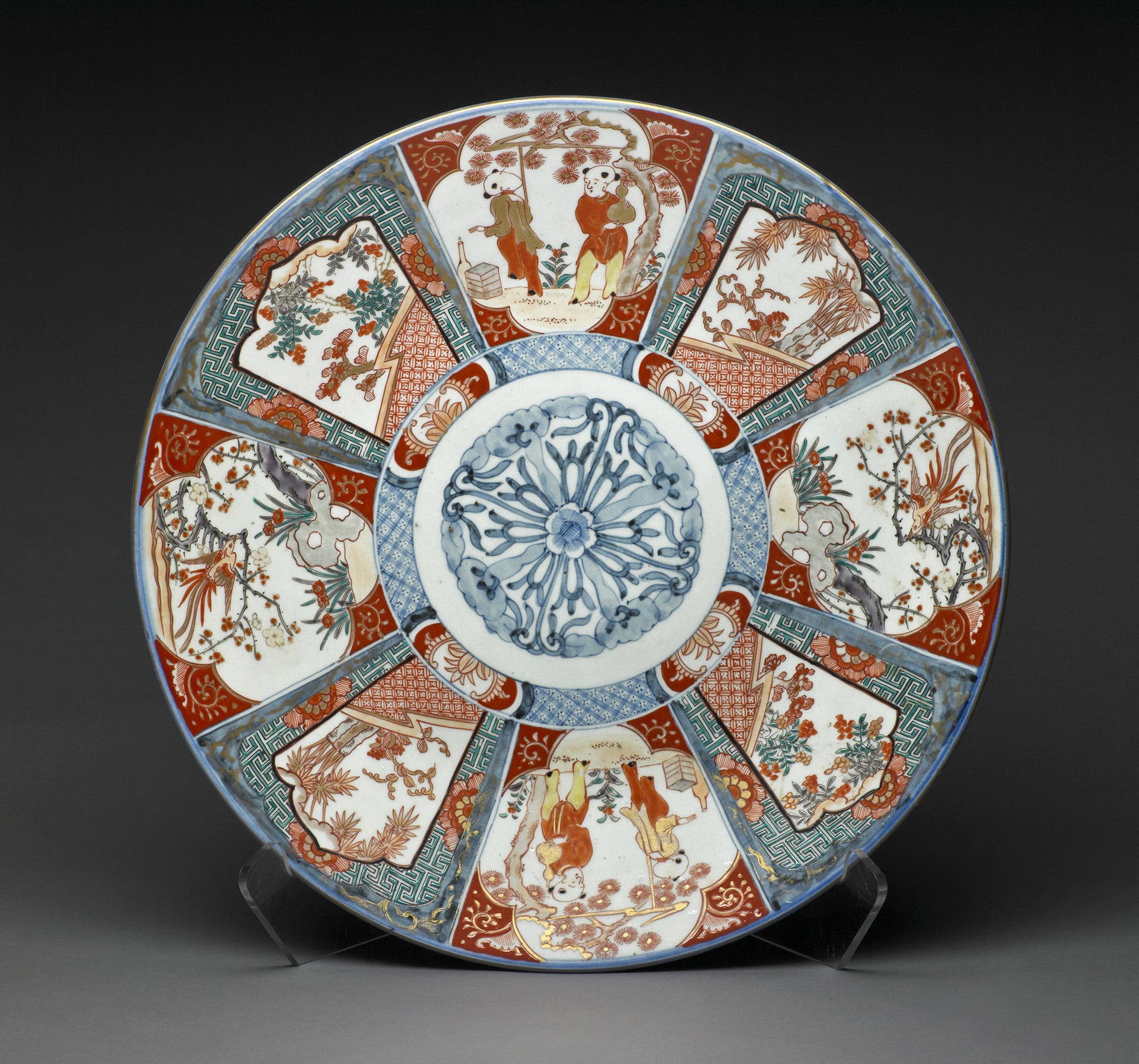 Circular porcelain plate with intricate blue floral center and alternating panels of red, blue, and white depicting traditional Asian figures and nature scenes.