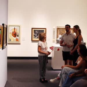 Female docent facing a group of people. She is holding a stick with a rocket-shaped sign that reads 