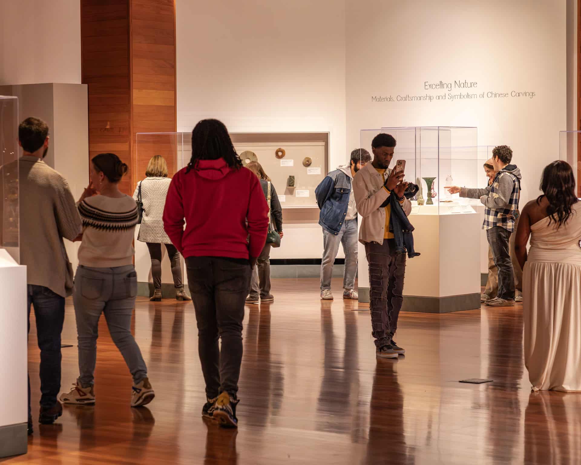 Museum attendees walking through the Asian wing galleries. Some are chatting, while some others are looking at the art or taking photos.