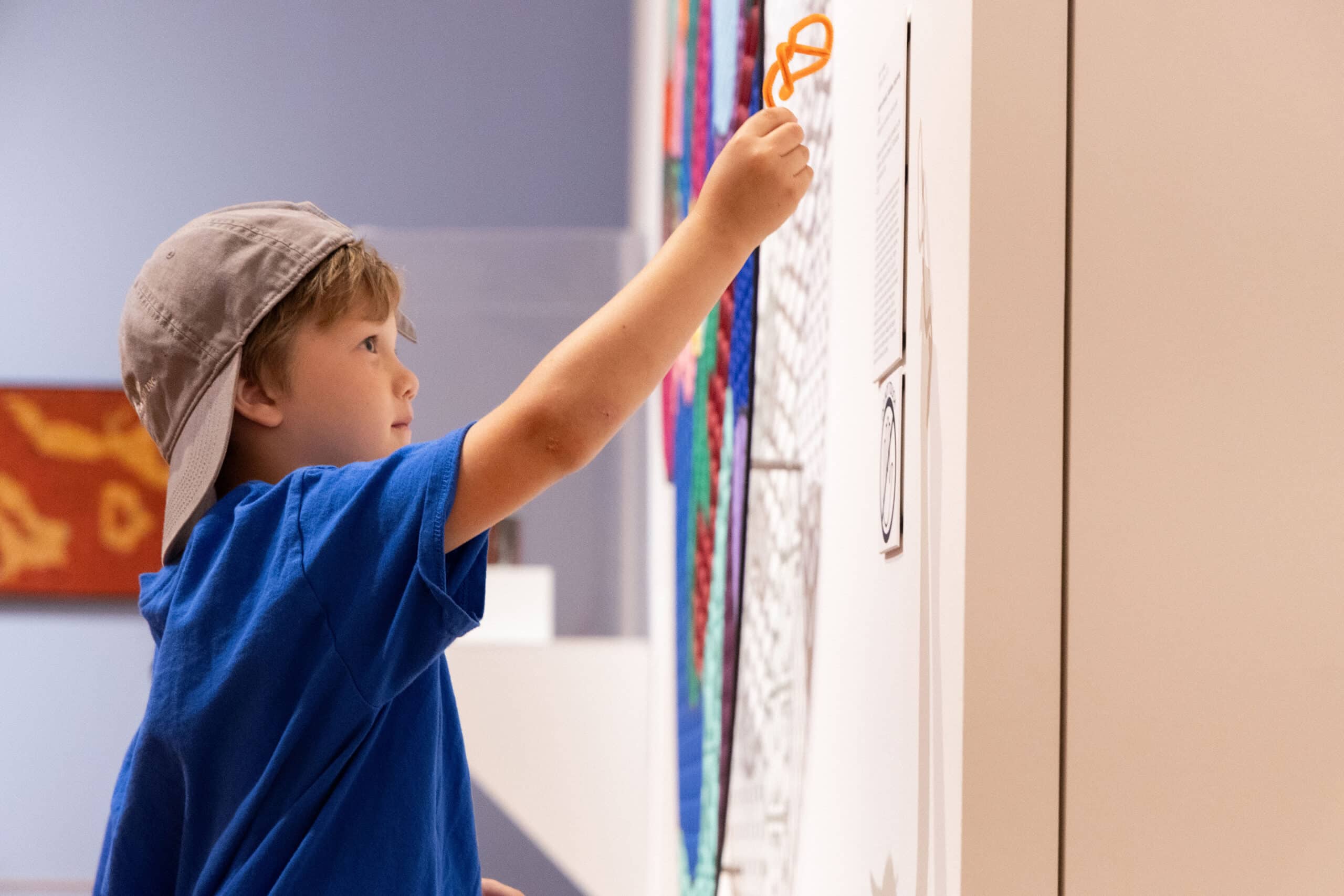 Young boy reaching up to point at the artwork with an orange shape during Tot Time. The artwork features colorful sections and outlines.