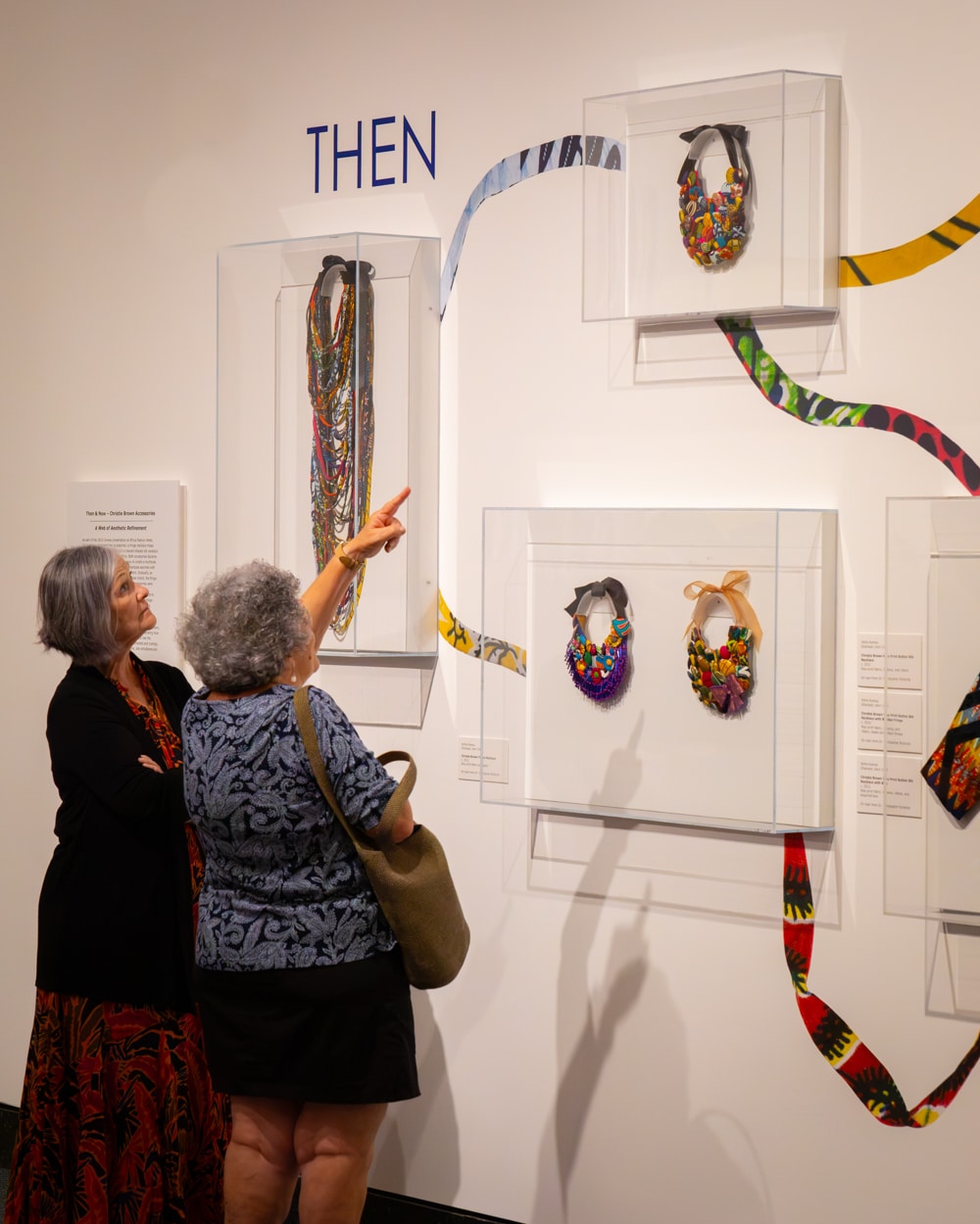 Two older ladies pointing at fashion pieces on a display case.
